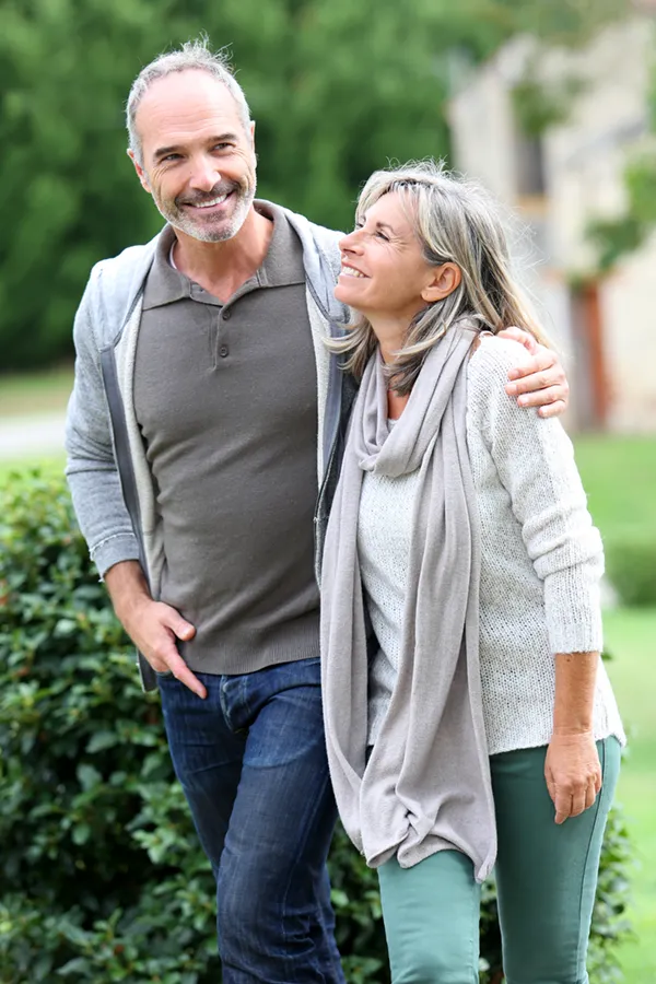 A mature couple in gray toned clothes and jeans walk happily outside, happy with their successful bioidentical hormone treatments from Tanya Zboril, NP of TBT Medical in Ottawa–Gatineau.