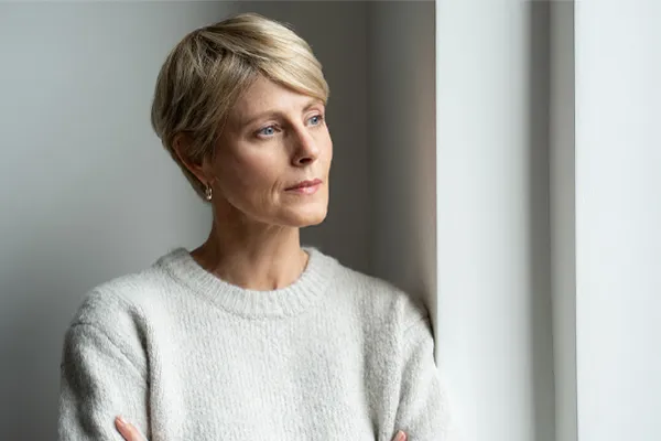 A blond, middle-aged woman looks out the window with a tired expression. Get chronic fatigue treatment from Tanya Zboril, NP of TBT Medical in Ottawa–Gatineau.