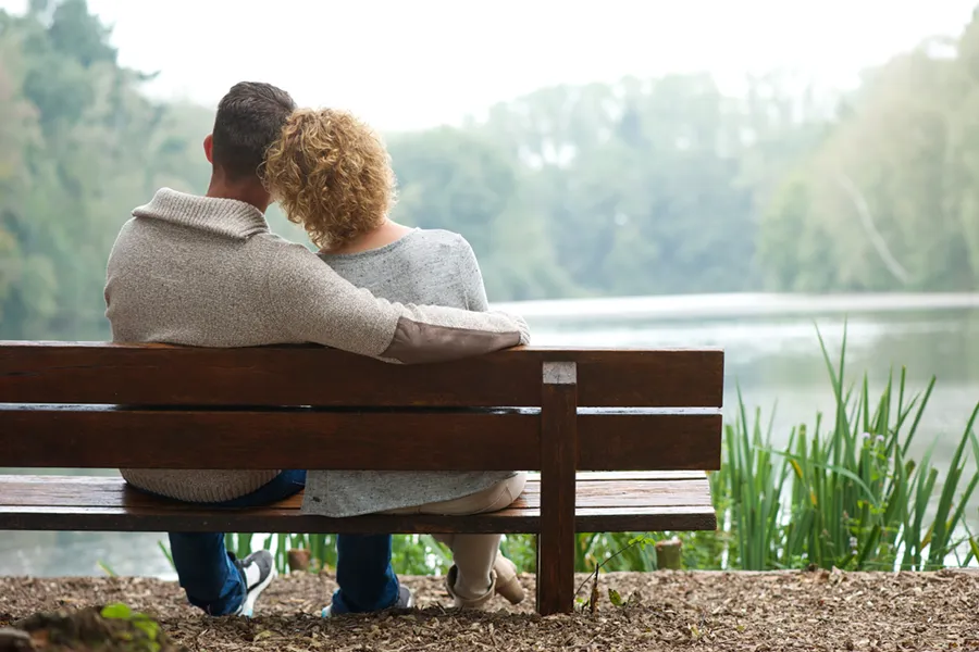 A couple wearing sweaters seen from behind sitting on a bench and looking out at a relaxing lake and forest, representing functional medicine treatment from Tanya Zboril, NP of TBT Medical in Ottawa–Gatineau.