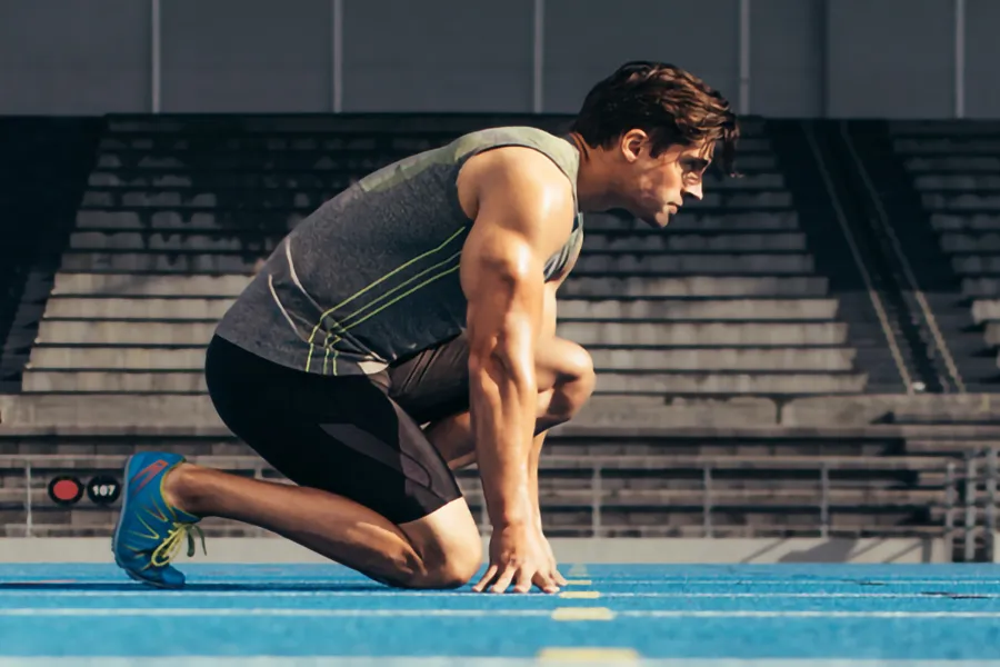 A white man kneels at the starting line on a track, determined to do his best. Get treatment for lean muscle loss and recovery from Tanya Zboril, NP of TBT Medical in Ottawa–Gatineau.
