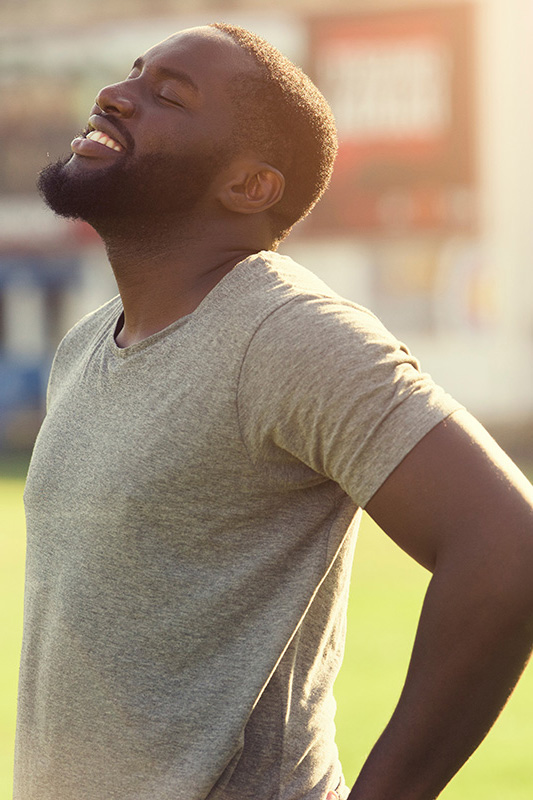 A black man in a gray t-shirt and smiles, looking up with closed eyes after a satisfying workout. Get treatment for lean muscle loss and recovery from Tanya Zboril, NP of TBT Medical in Ottawa–Gatineau.