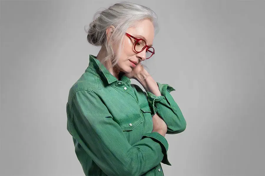 A middle-aged woman in a green shirt holds her neck and grimaces in pain. Schedule low dose naltrexone treatment from Tanya Zboril, NP of TBT Medical in Ottawa–Gatineau.