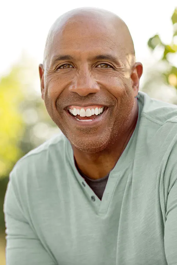 A man in a green shirt sits outside smiling and pain-free. Get low dose naltrexone treatment from Tanya Zboril, NP of TBT Medical in Ottawa–Gatineau.