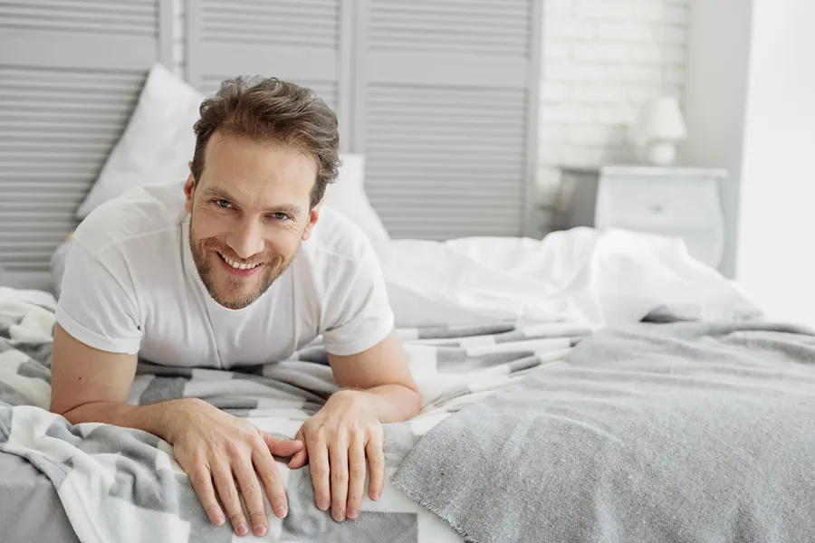 Low-Libido-in-Men-Doctor A dirty-blonde haired man lays on his stomach in bed smiling. Schedule treatment for low libido in men from Tanya Zboril, NP of TBT Medical in Ottawa–Gatineau.