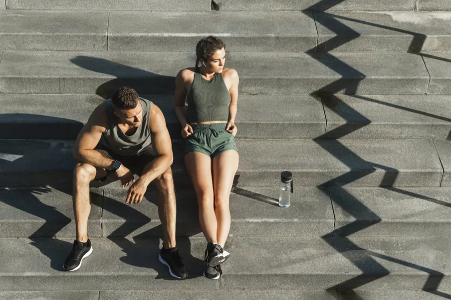 Medical-Weight-Loss-Doctor A couple in gray and green track clothes resting after a workout on stone steps, happy with their weight loss plans from Tanya Zboril, NP of TBT Medical in Ottawa–Gatineau.