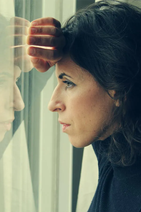 A brunette woman in a thin dark turtleneck looks out the window with a serious expression, suffering from PCOS. Get treatment for Polycistic Ovarian Syndrome/PCOS from Tanya Zboril, NP of TBT Medical in Ottawa–Gatineau.
