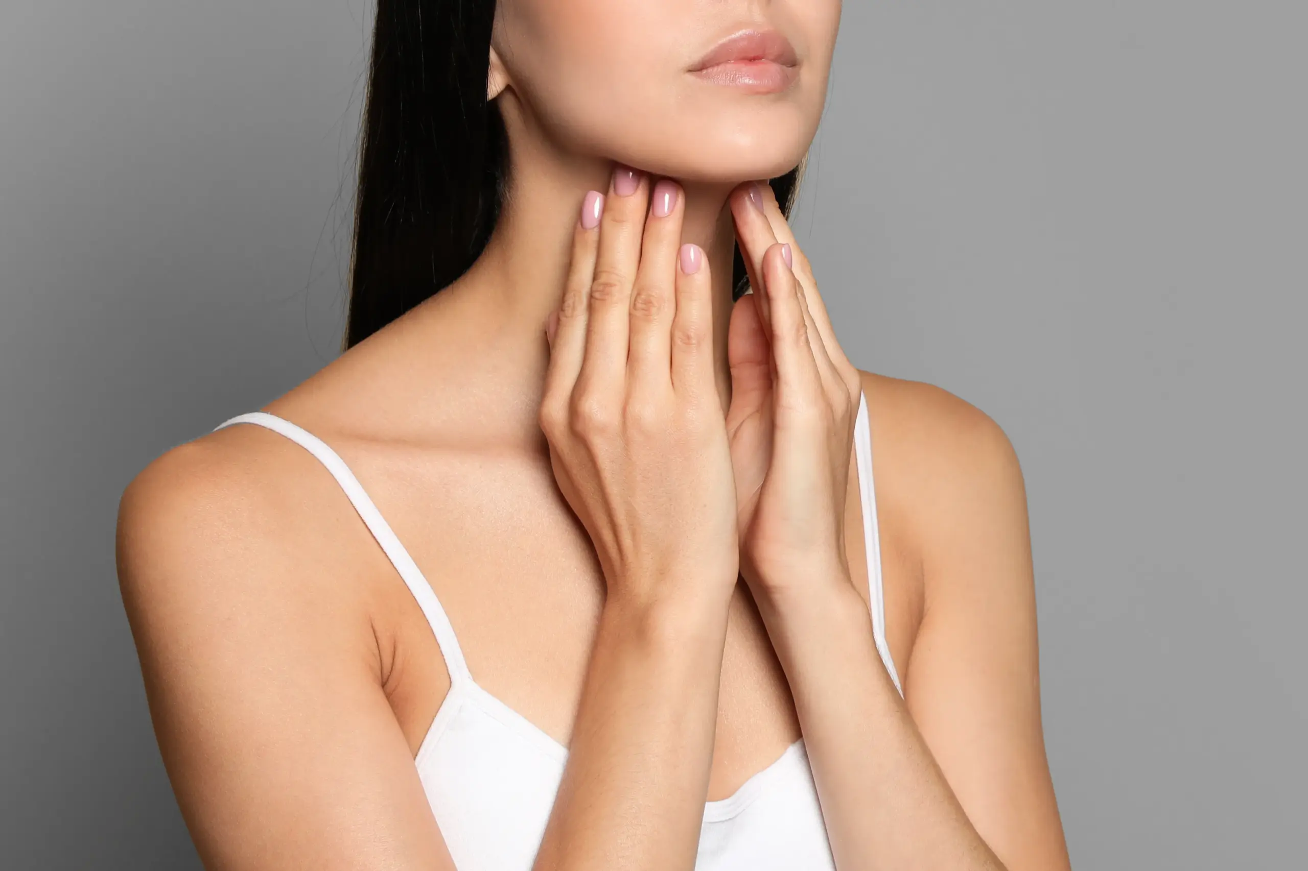 A woman in a white tank top touches her neck looking for signs of thyroid disorder. Get help for thyroid disorders from Tanya Zboril, NP of TBT Medical in Ottawa–Gatineau.