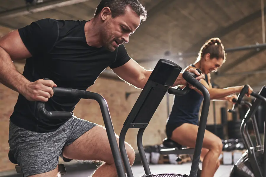 Tirzepatide-Doctor A couple in a brick gym work as hard as they can on exercise bikes, inspired by successful Tirzepatide treatment from Tanya Zboril, NP of TBT Medical in Ottawa–Gatineau.