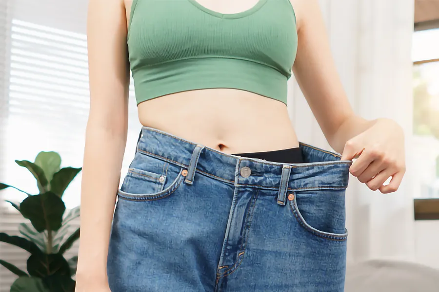 Zepbound-Weight-Loss-Clinic A close-up of a young woman in a green crop top, holding out her oversized blue jeans to show significant weight loss. Zepbound Weight Loss Injections offered by Tanya Zboril, NP of TBT Medical in Ottawa–Gatineau.